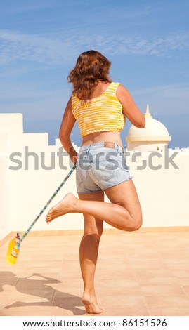 tanned middle-aged woman in shorts and crop top  on the sunroof,dancing with a broomstick