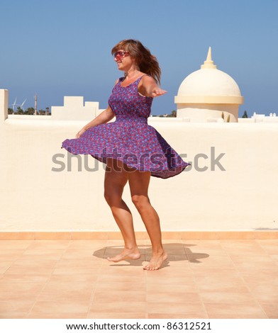 age doesn\'t matter - tanned, fit middle-aged woman dances on the sunroof in short flared dress