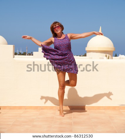 age doesn't matter - tanned, fit middle-aged woman dances on the sunroof in short flared dress