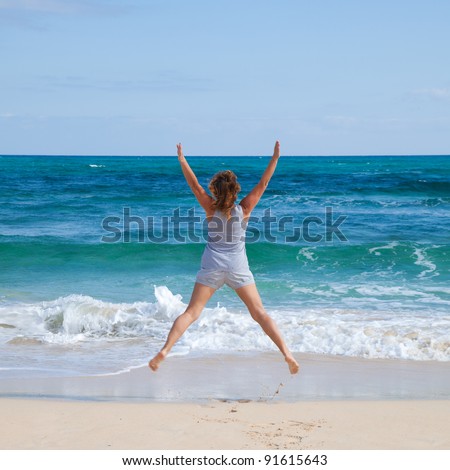jumping by an ocean - happy tanned middle-age woman jumping in the shallow water