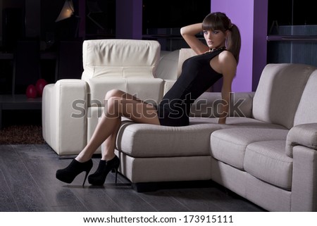 Long legged girl posing on a white leather couch while holding her hair in a pony tail