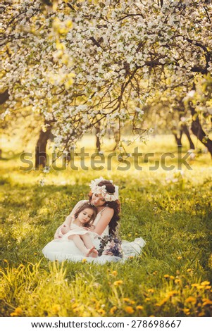 mom and little girl sits in a blooming garden on a sunny day.