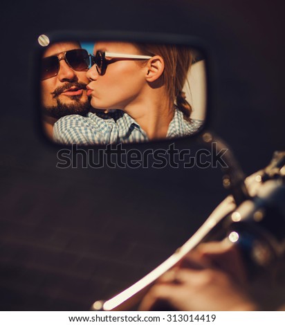 carefree young couple in sunglasses kissing reflected in the mirror of a motorcycle