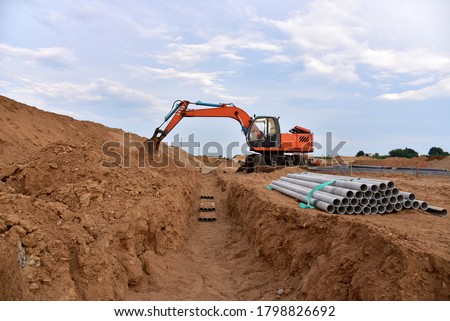 Excavator dig the trenches at a construction site. Trench for laying external sewer pipes. Sewage drainage system for a multi-story building. Civil infrastructure pipe, water lines and sanitary storm