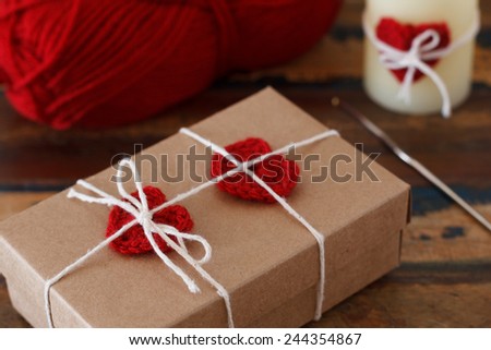 Saint Valentine decoration: handmade crochet red heart on gift paper box and candle. Selective focus