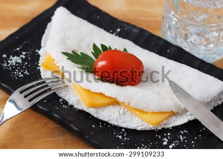 Casabe (bammy, beiju, bob, biju) - flatbread made from cassava (tapioca) with cheese, cherry tomato and parsley on black plate. Selective focus. Copy space