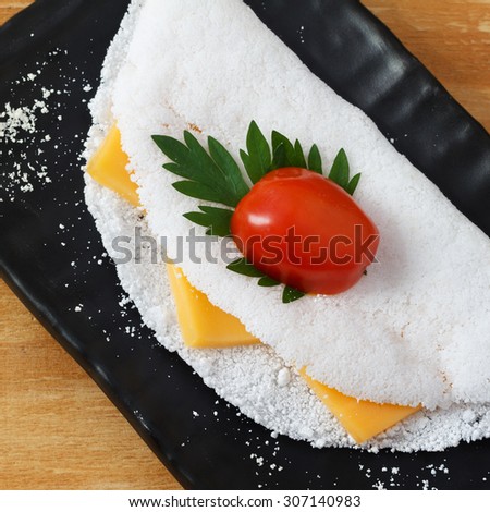 Casabe (bammy, beiju, bob, biju) - flatbread made from cassava (tapioca) with cheese, cherry tomato and parsley on black plate. Selective focus