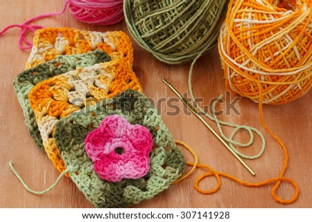 Handmade colorful crochet granny afghan square with skein on wooden table. Selective focus