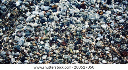 Grey and black pebbles on the riverbed. Aged photo. Smooth stones under water. Toned effect. Sunlight on the water surface. Vintage effect image. Cirali, Antalya Province, Turkey.