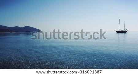 Sailing ship profile. Toned image. Sunbeams on the sea surface. Morning sea with boat on the horizon. Aged photo. Calm Sea with a Sailing Vessel. Cirali, Antalya Province, Turkey.