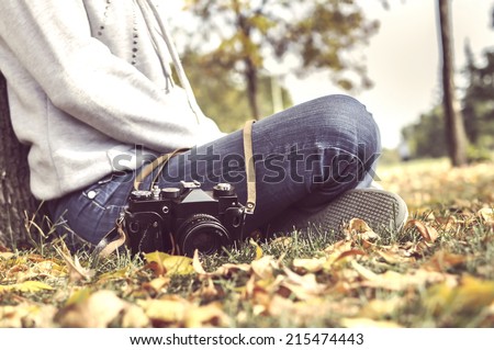 vintage autumn photo with girl sitting in a park with old camera