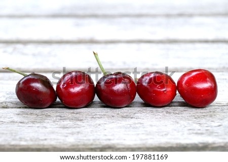 Five freshly picked bright red cherries lined up on a wooden picnic table