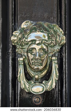 Metal door knocker shaped as a human head on black door