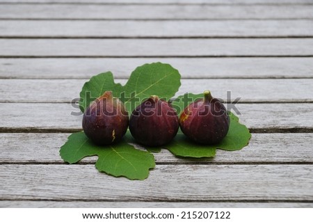 Three purple figs on a fig leaf and wooden table background