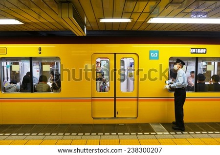 TOKYO, JAPAN --NOVEMBER 2014-- A guard wearing a health mask pushes riders into a yellow Tokyo subway, which can get very crowded with Japanese commuters during rush hours.