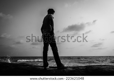 Man standing alone on a rock at the beach,Black and white