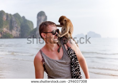 Young man with funny monkey sitting on his shoulder, touching his nose, tropical country