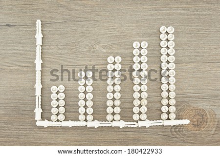 Screws and wall plugs placed as bar chart on dark brown wood background.