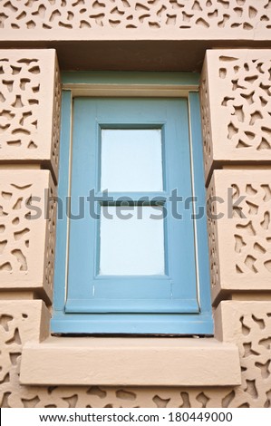 Blue square window in brown wall of the building, which is located at Grand Palace
