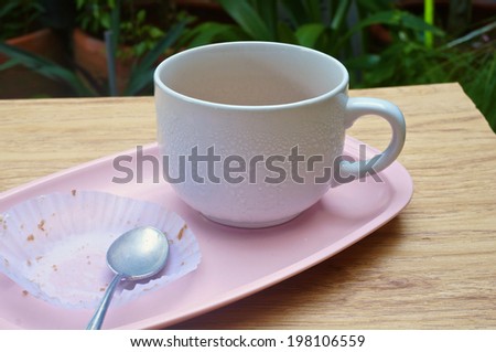 Eaten cake with tea in white cup with spoon put on pink tray in garden.