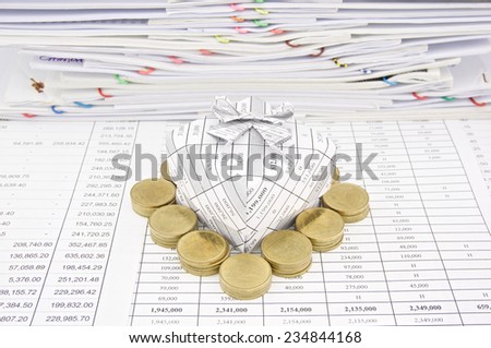 Pile of gold coin around gift box place on finance account with pile of paperwork as background.