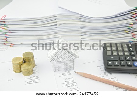 House near gold coin on balance sheet and pencil with pile of paperwork as background.