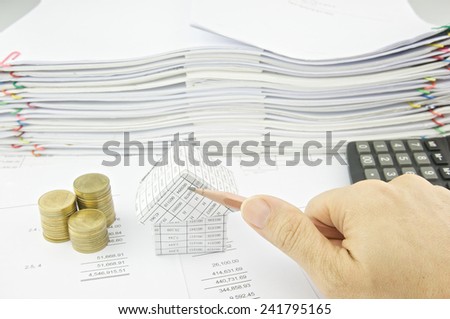 Man is holding pencil slantingly over balance sheet with pile of paperwork as background.