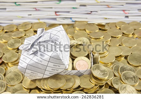 Gift box in heap of gold coins  with pile of paperwork as background.