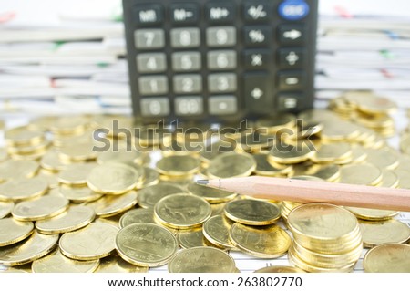 Close up pencil on heap of gold coins with calculator and pile of paperwork as background.
