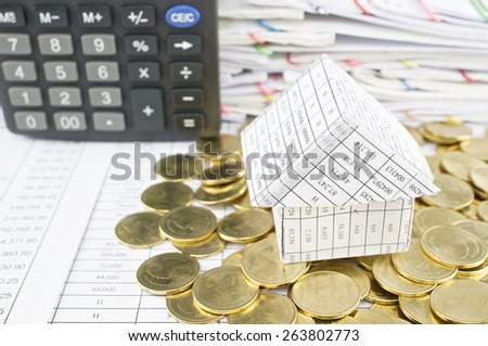 Close up house on heap of gold coins with calculator and pile of paperwork as background.