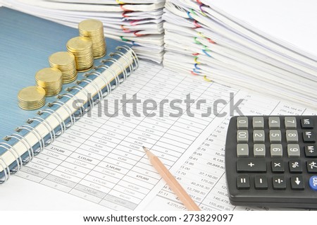 Pencil and gold coins on notebook with calculator on finance report with pile of paperwork as background.