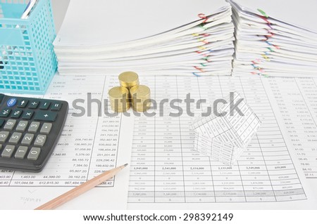Pencil with house and calculator with pile of gold coins on finance account with pen in blue basket with pile of paperwork as background.