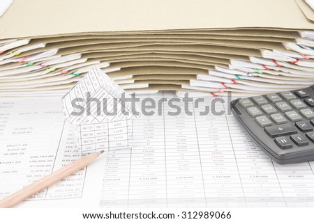 House and pencil with calculator on finance account have brown envelope between overload of old paperwork as background.
