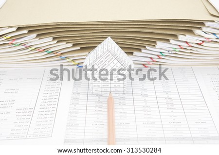 Brown pencil point to house on finance account have brown envelope between overload of old paperwork as background.