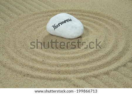 stone onto sand with patterns and the German word Harmonie means harmony