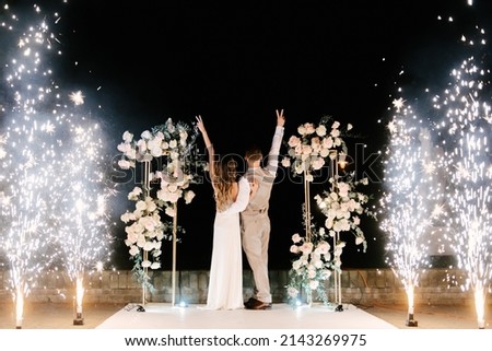Young bride and groom stand near the wedding arch at night with lights, smoke and fireworks, silhouettes of the newlyweds Photo stock © 