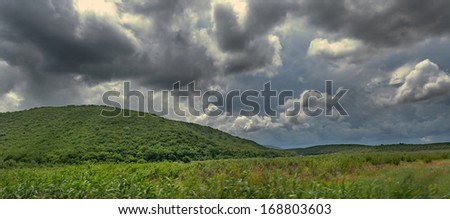 Summer field, mountains, forest and dramatic sky before a thunderstorm