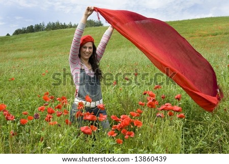 Beautiful girl standing among red poppies and holding a red scarf