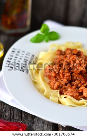 Pasta Bolognese in the white plate with letters, with basil leaf. Little bowl of olive oil and chili pepper on the white napkin on the old wooden table