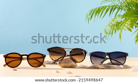 Sunglasses summer sale concept. Different sunglasses on a beach with green palm leaves. Trendy Fashion summer accessories. Copy space. Optic store. Vacation, travel concept. Sunglass offer banner Stock foto © 