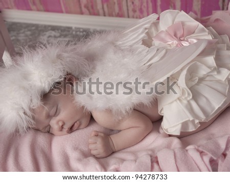 Newborn baby girl with feathered halo and wing\'s asleep in her bed she look\'s like and angel.