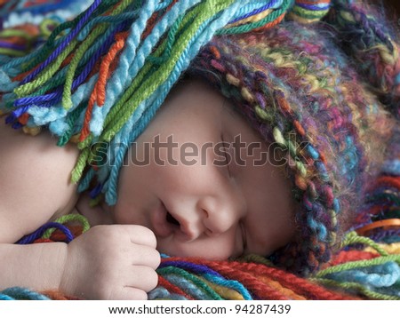 Sleeping newborn baby boy one week old with blue and white hat. He is laying on a blanket of multicolored yarn. He has a matching hat.