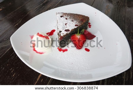 Piece of chocolate cake with powdered sugar, ice cream and fresh berry on wooden background.