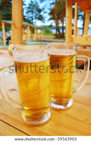 Two mugs of beer staying on the wood table in outside bar.