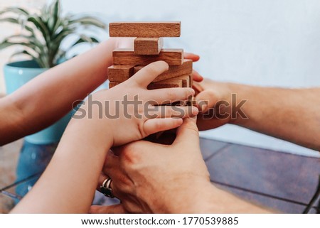 Father and child playing game tumble tower from wooden block. Man's and kids hands hold the tower together to prevent fall and crisis. Man helps child win. Concept of support and mutual assistance 商業照片 © 