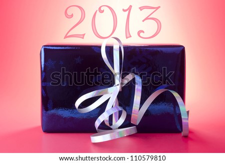 2013 New Year present or gift wrapped in blue shiny wrapping paper with silver curly ribbon against red background.