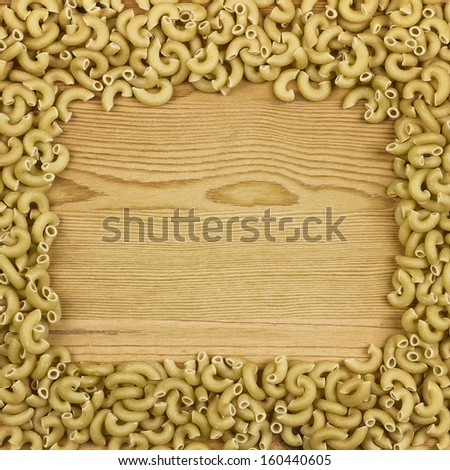 Textured wood background with yellow macaroni pasta border frame with copy space.