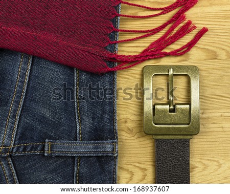 Fashion blue denim jeans red scarf and brown leather belt on rustic wood background.