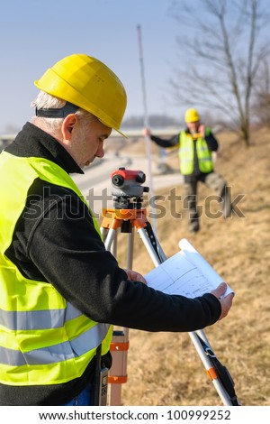 Land surveyors on highway reading geodesist plans use tacheometer