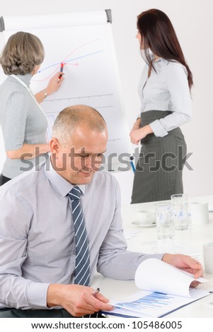 Giving presentation mature executive during meeting woman pointing flip chart